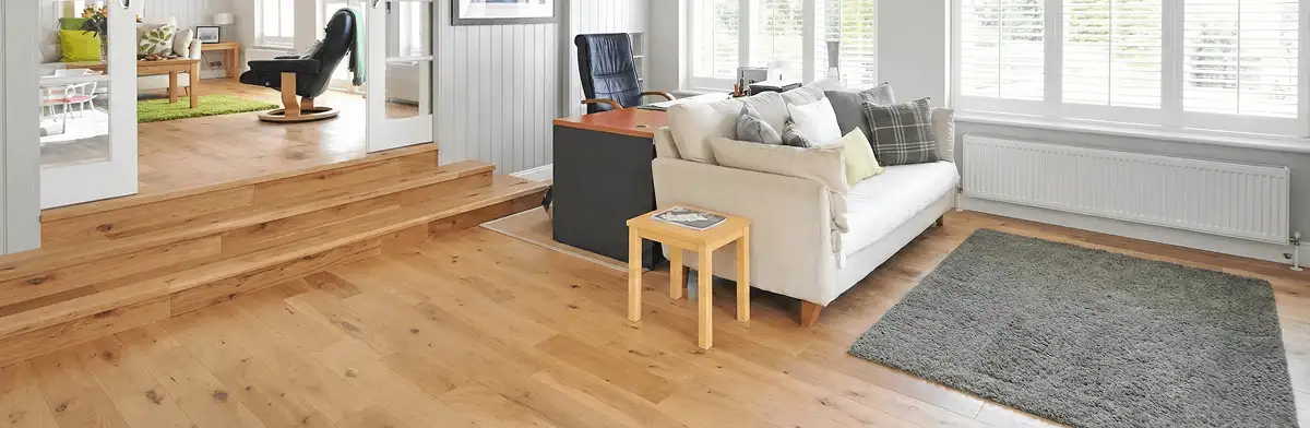 A modern living room with professionally installed laminate flooring, a beige sofa, a small side table, a gray rug, and large windows with white shutters in Glendale, AZ
